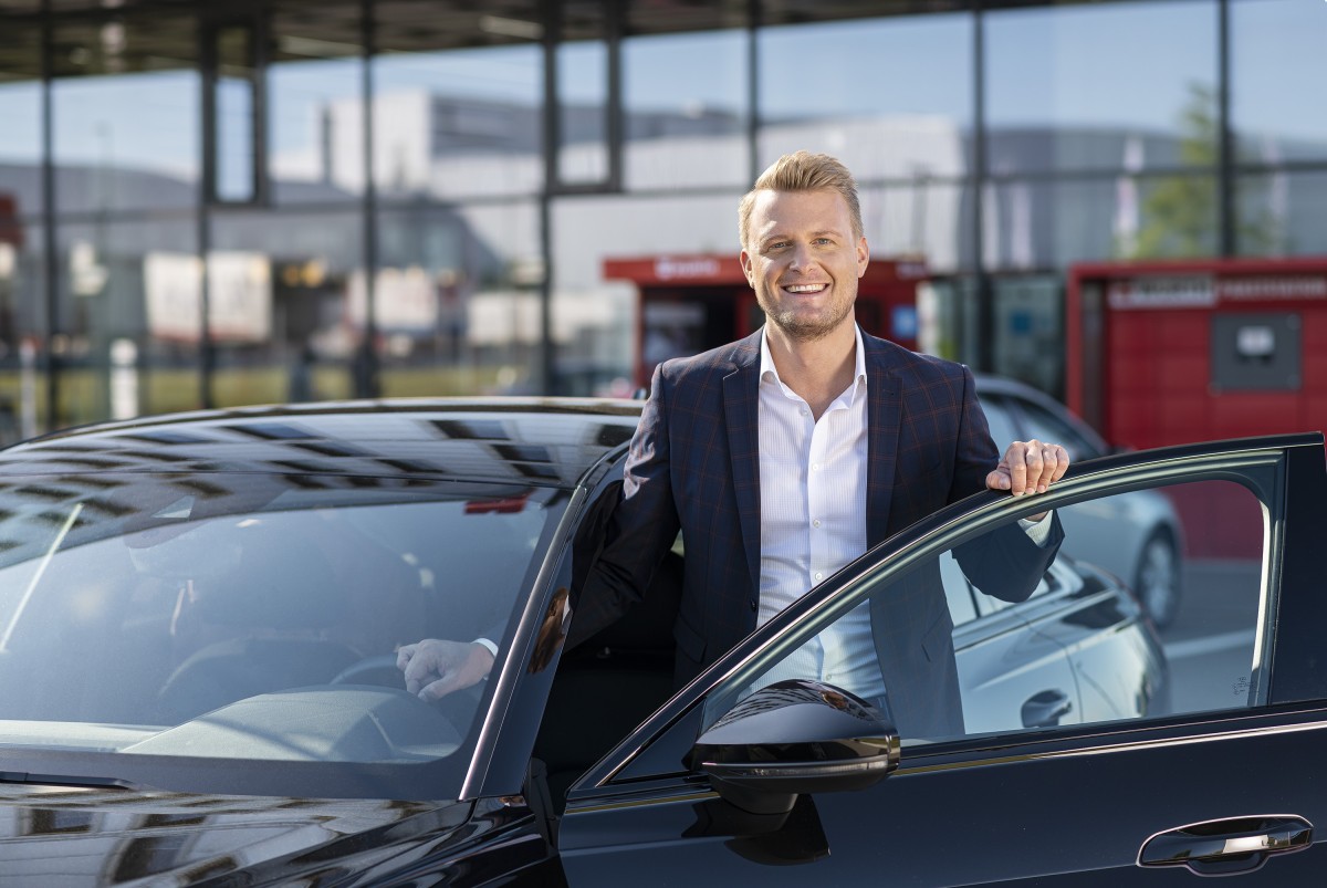 Mann steht am Auto bei geöffneter Autotür